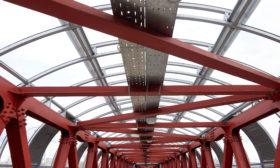 The roof is made of steel channels connected to each other. Red iron beams on bolts and rivets. Crosswalk, construction.